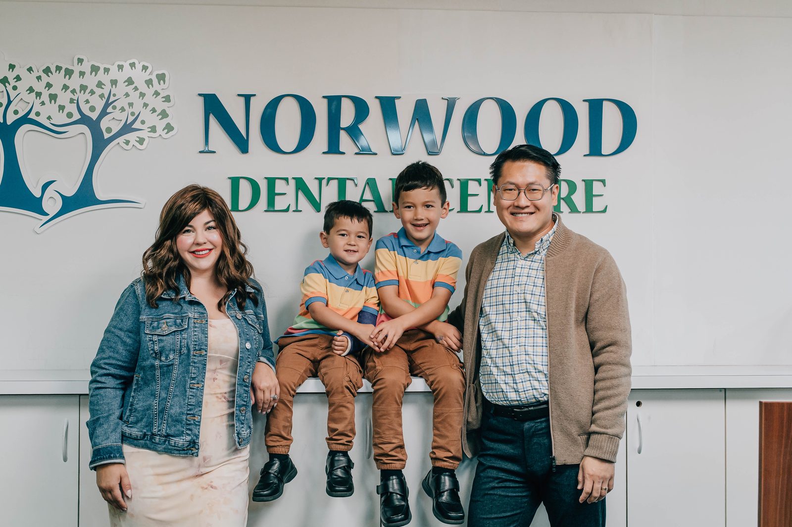 The Chin family in front of the Norwood Dental Centre brand wall